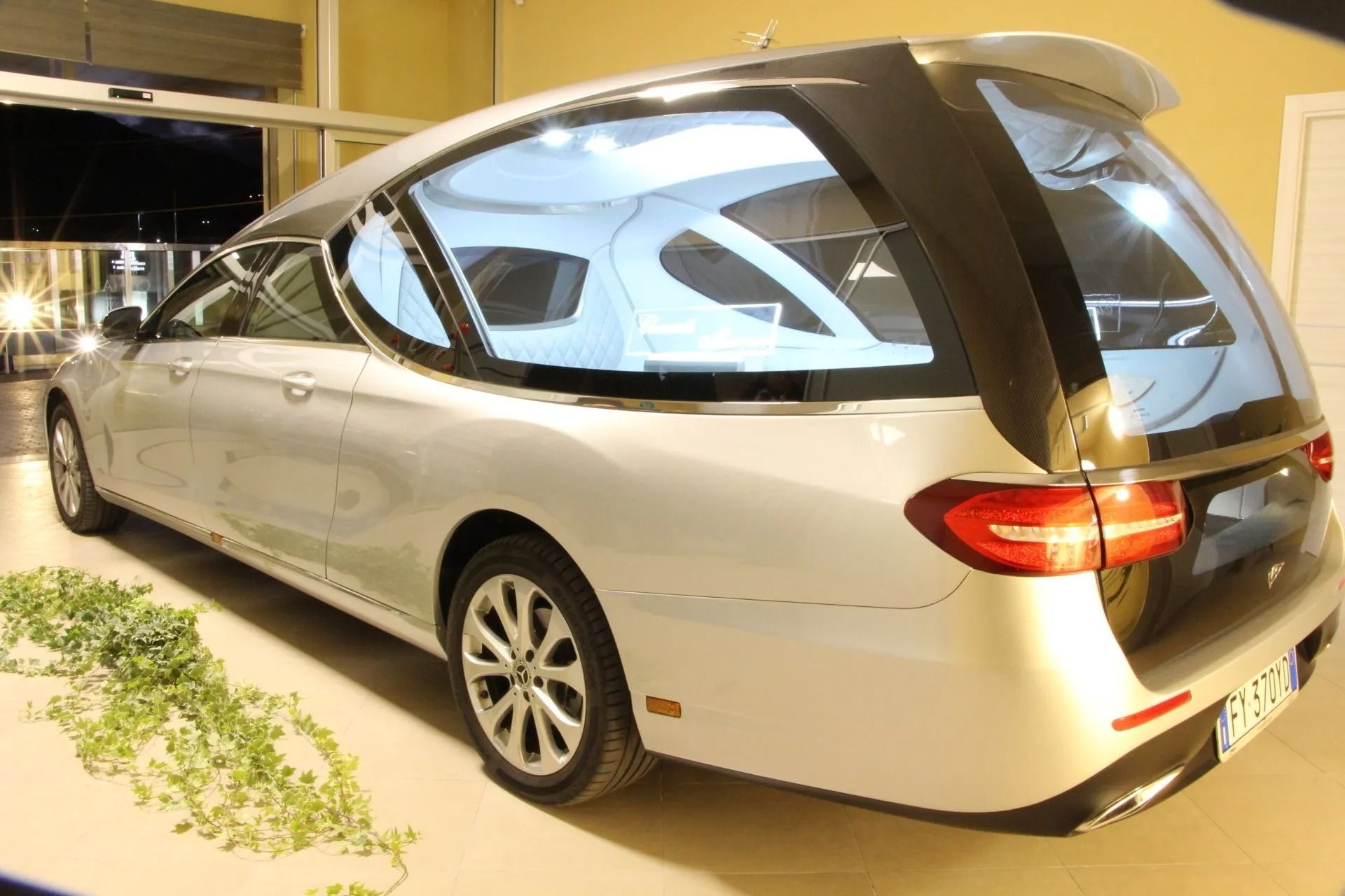 Silver futuristic concept car on display indoors, viewed from the rear side.