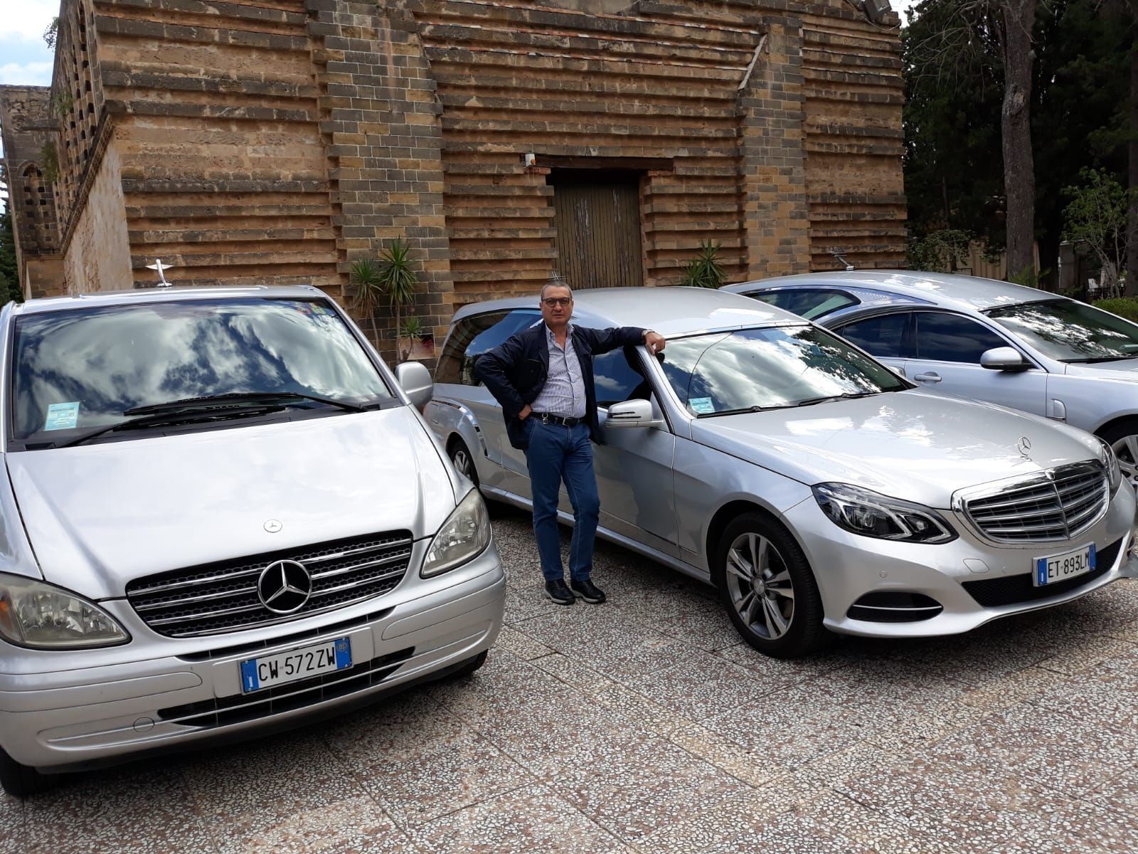 Three silver cars parked by a log cabin, with a man standing between two cars.