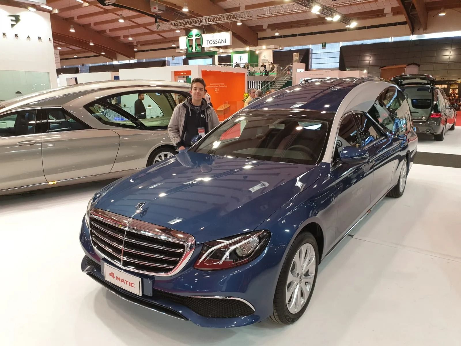 Blue Mercedes sedan displayed at an indoor auto show, with a man standing beside it
