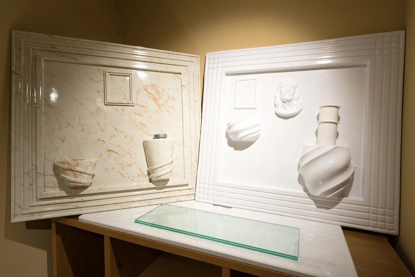 White framed wall art with plaster relief sculptures of vessels and faces in a gallery-like setting