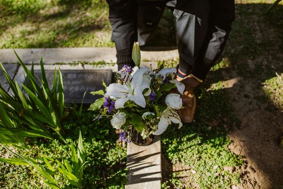 Person holding a white flower bouquet over a gravesite in bright sunlight