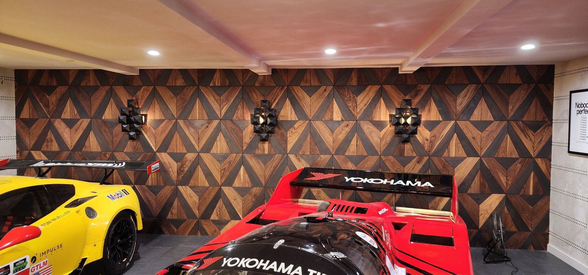 Indoor garage with two race cars, a yellow car on the left and a red car in front of patterned wall decor.