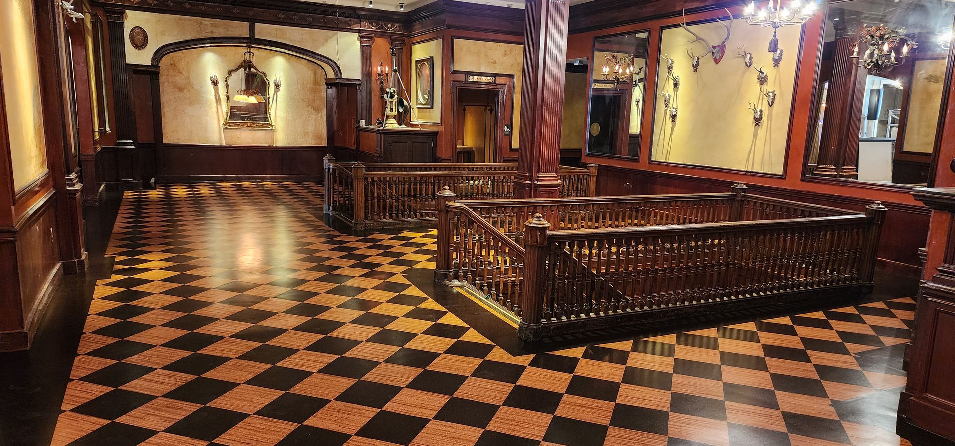 Elegant interior hall with black-and-tan checkered floor, wood railings, and warm wall sconces