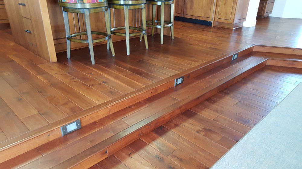 Indoor wooden floor with a raised step and short ramp, marked by small blue plates near a dining area