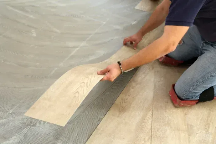 Person kneeling, peeling up a wood-look vinyl floor plank during installation or removal
