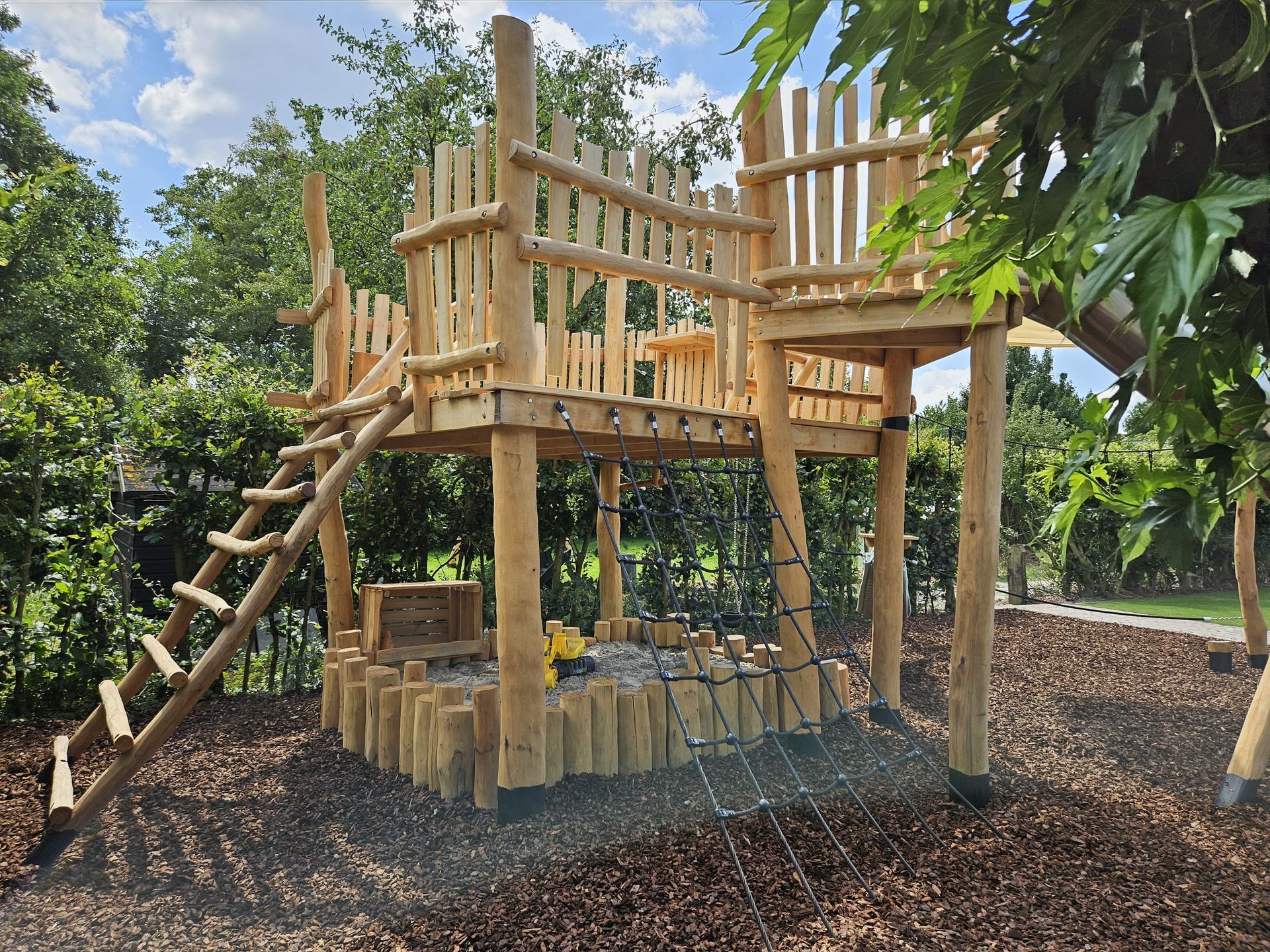 Houten speeltoestel met ladder, platform en boomstammen op houtsnippers, voor buiten.