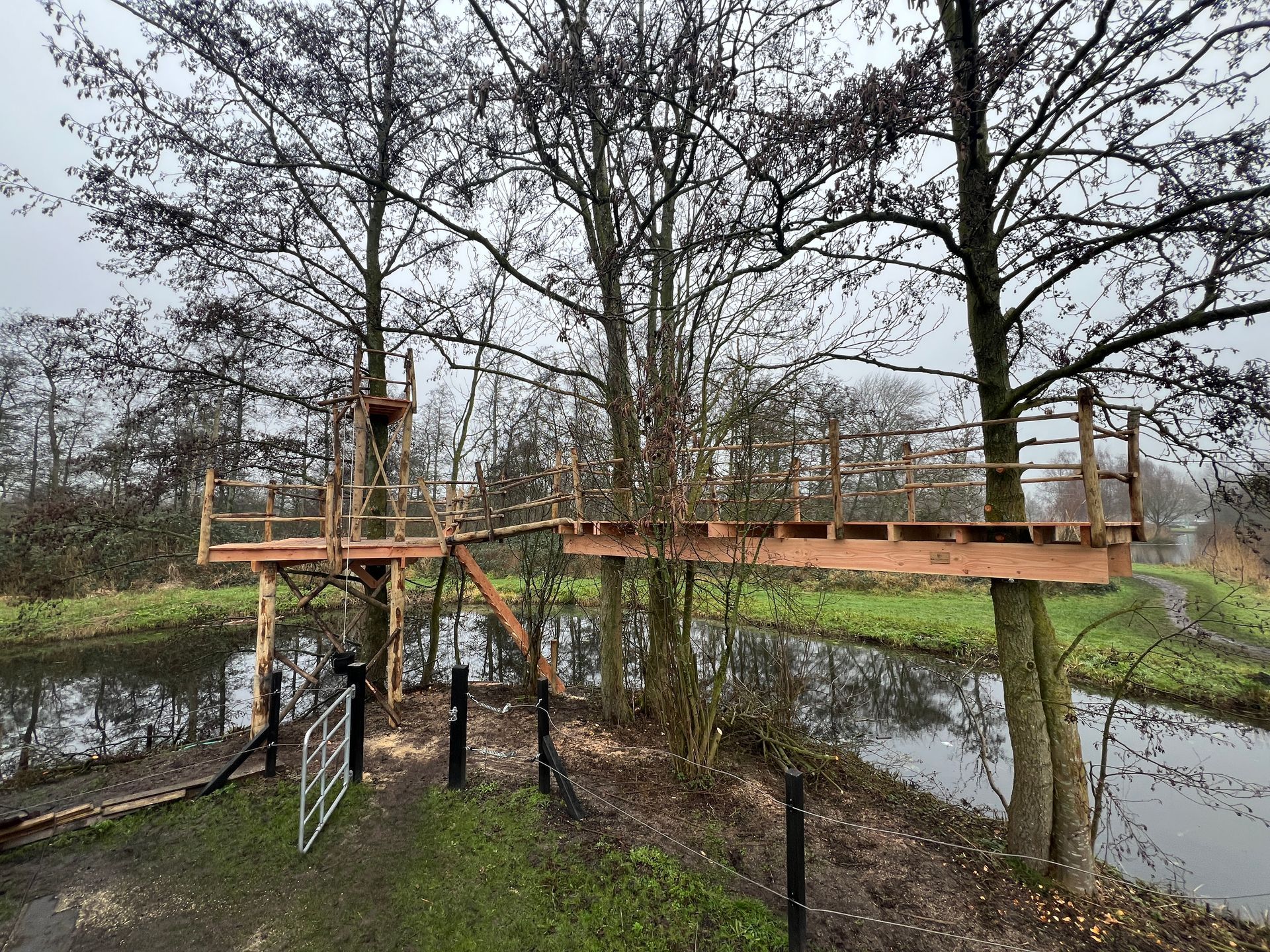 Houten boomhutplatformen die met elkaar verbonden zijn door een brug over een waterpartij.