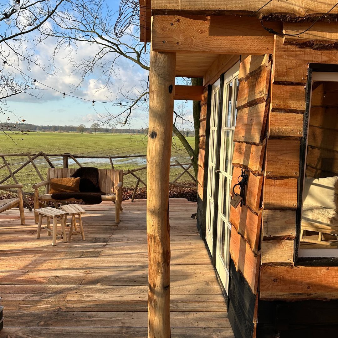 Houten boomhut met een veranda die uitkijkt over een veld.