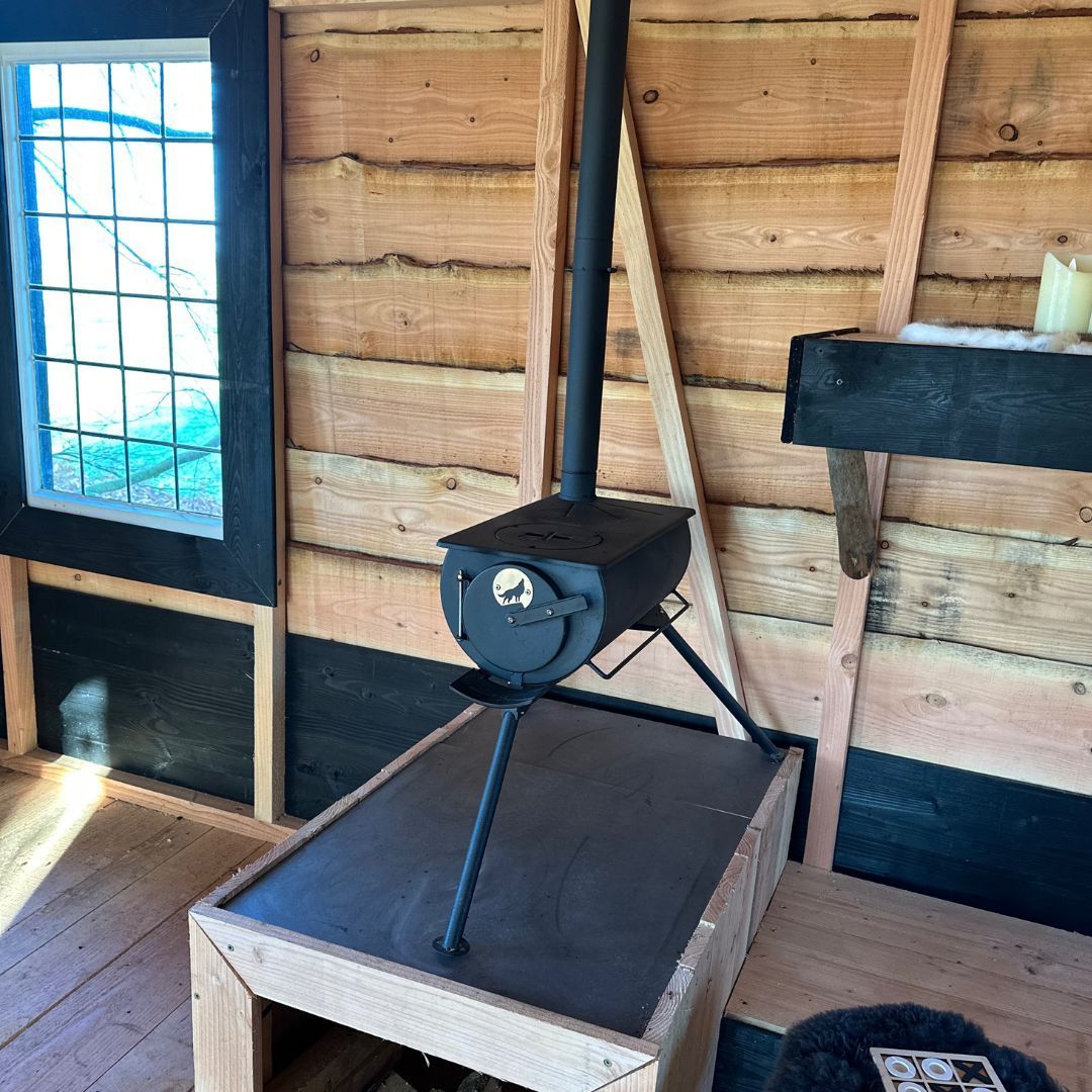 Een kleine houtkachel in een houten hut, naast een raam.