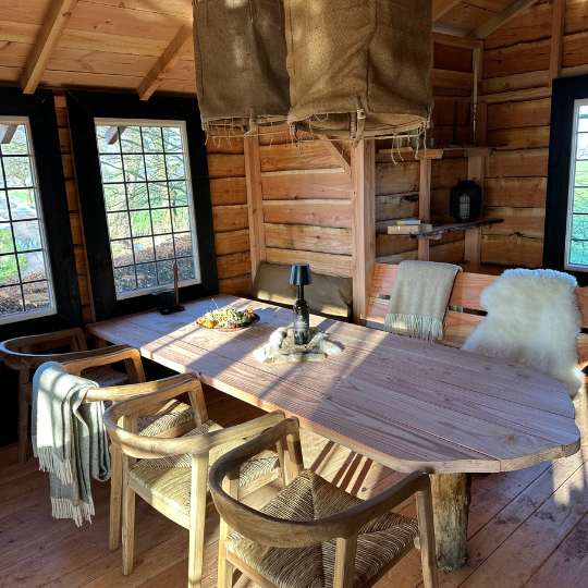Houten interieur van een blokhut met eettafel, banken en stoelen bij de ramen.