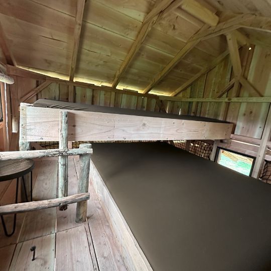 Houten stapelbedden in een rustieke hut. Het bovenste bed is leeg. Bruine matrassen.