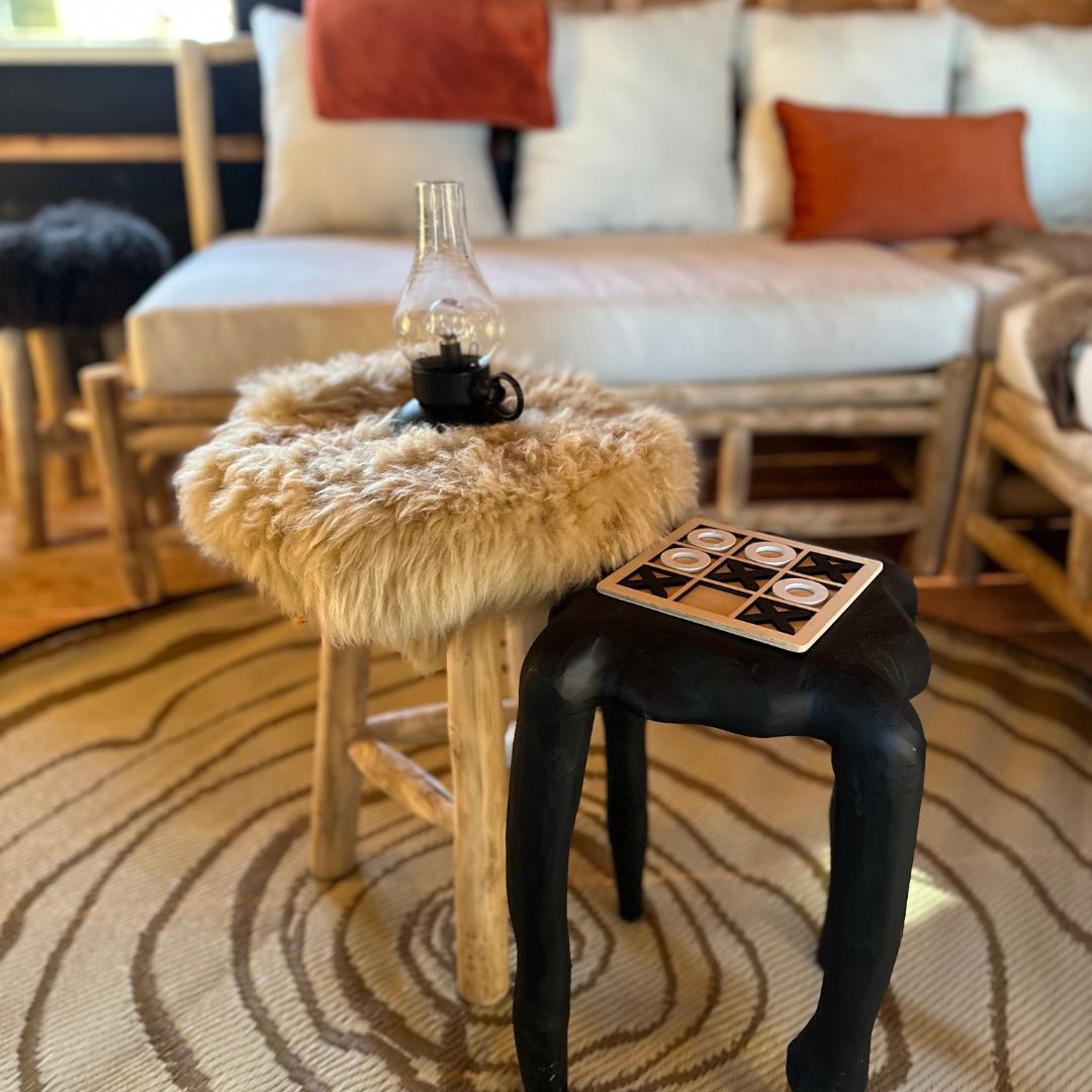 Gezellige boomhut met meubels, een vloerkleed en kussens. Twee krukjes, waarvan één met een schapenvacht, en een lamp.