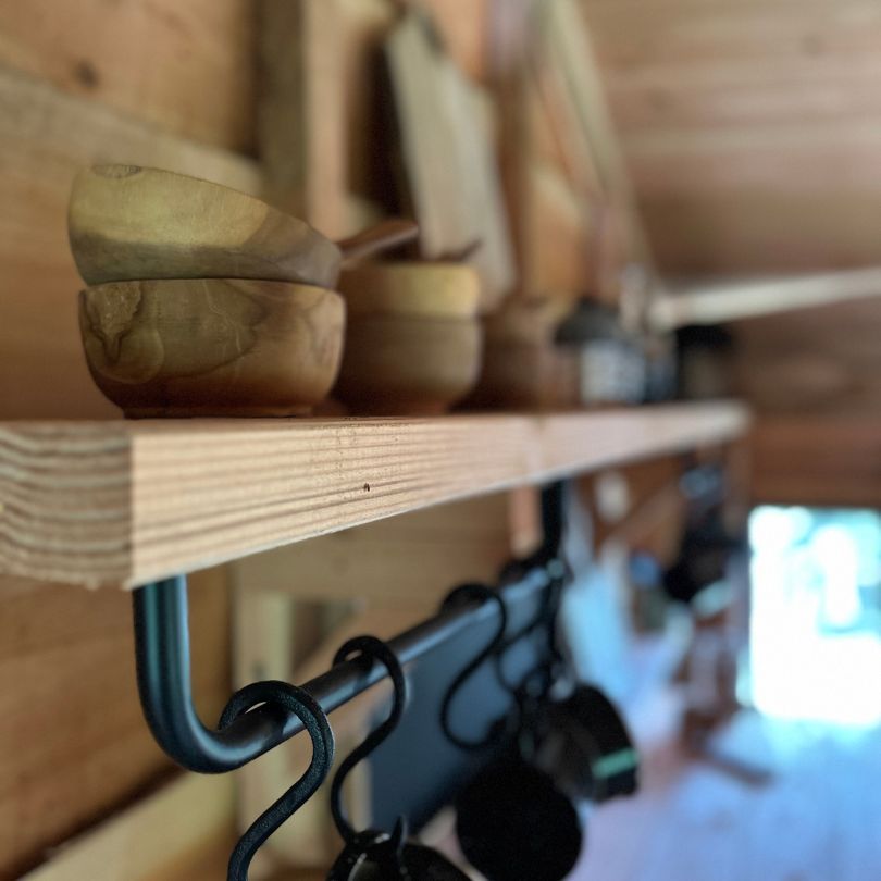 Houten kommen op een houten plank, boven hangende potten en pannen, in een rustieke keuken.