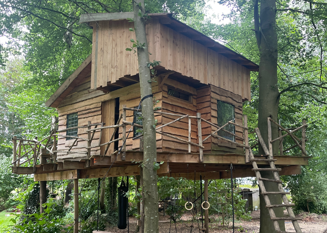 Houten boomhut met ladder, leuning en steunpalen, gebouwd in een bos.