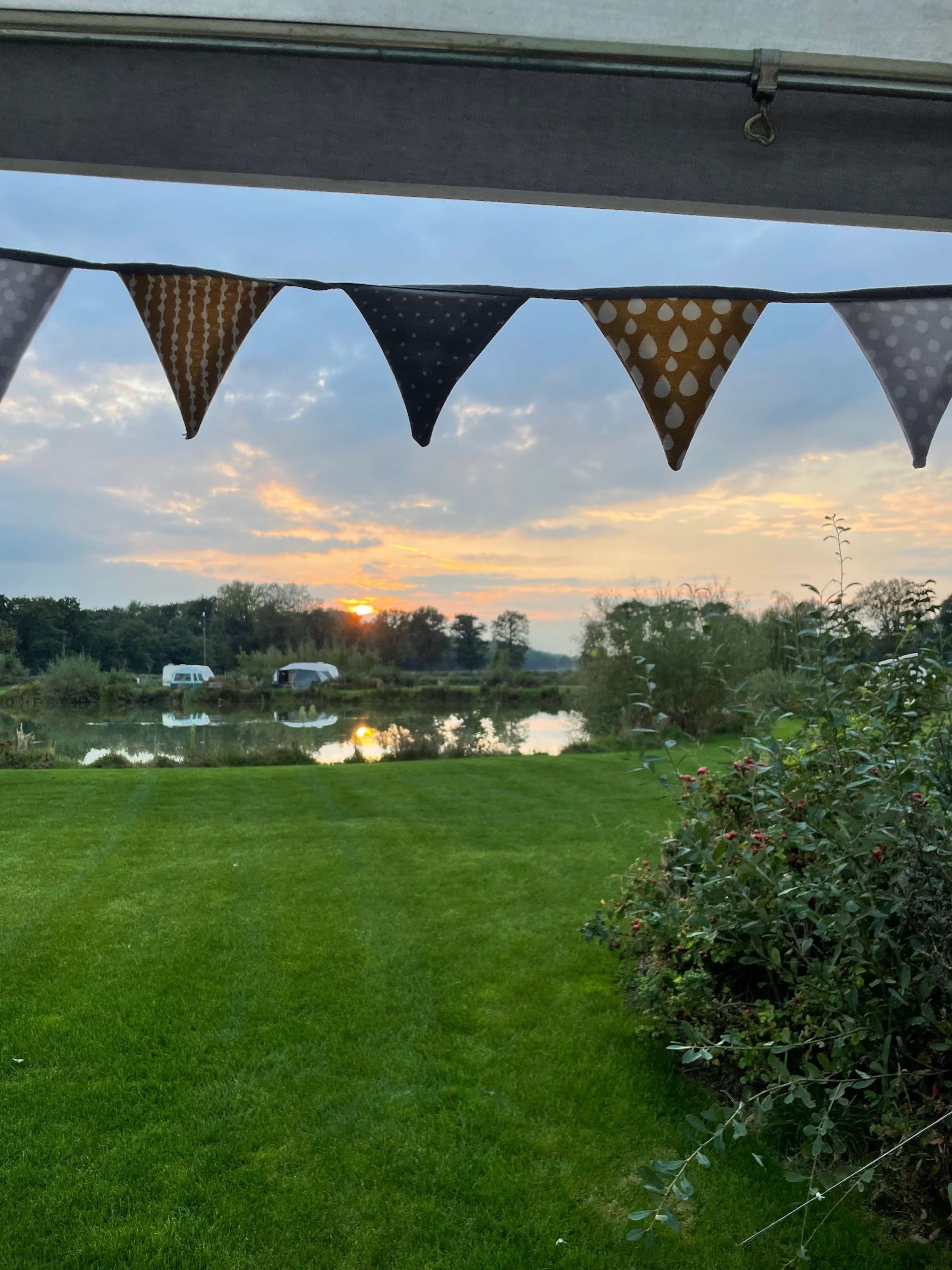 Een slinger hangt boven een groen gazon met een meer en een zonsondergang op de achtergrond.