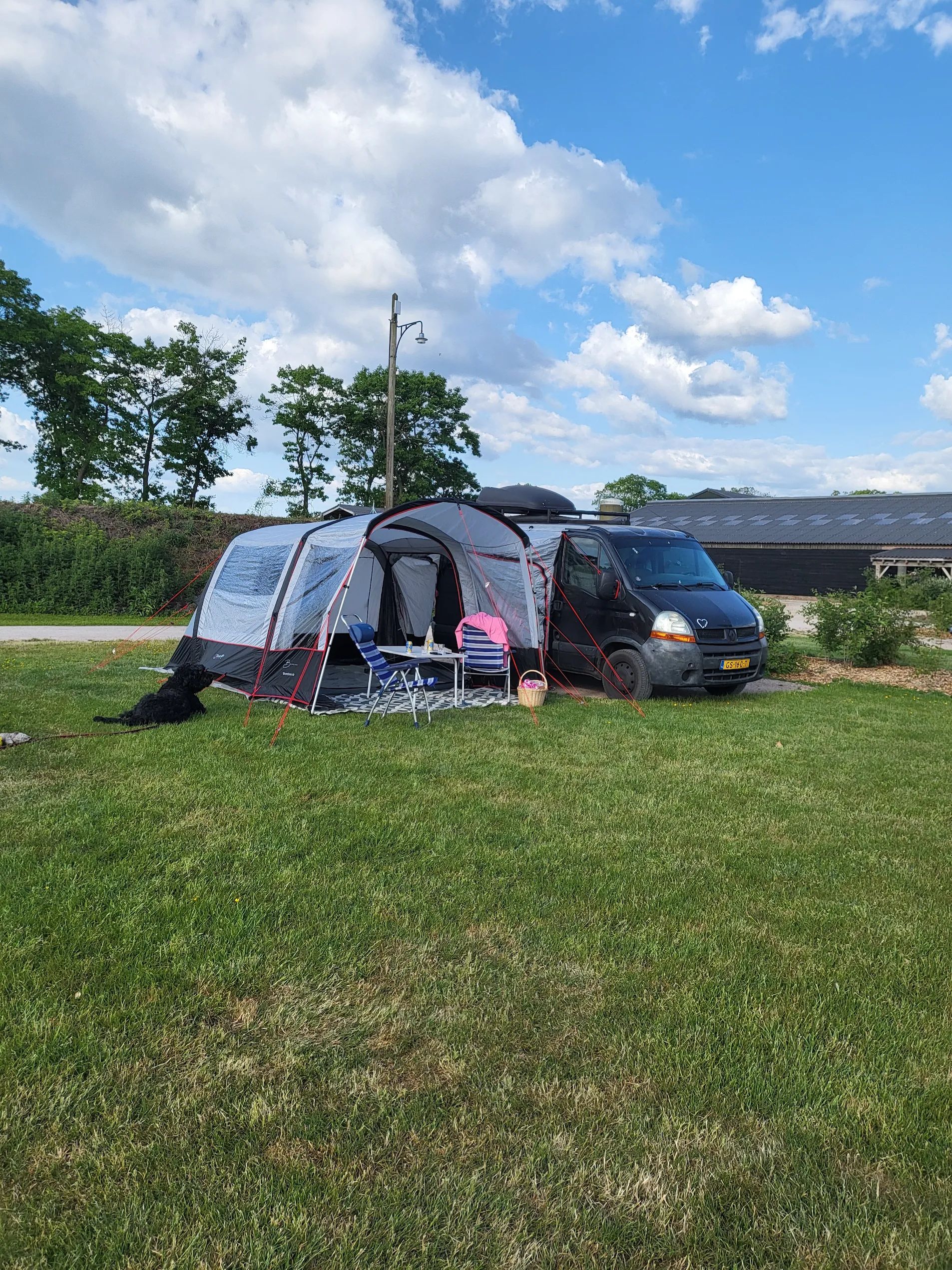 Op een zonnige dag staat een zwarte bestelwagen met een bijbehorende tent geparkeerd op een grasveld.