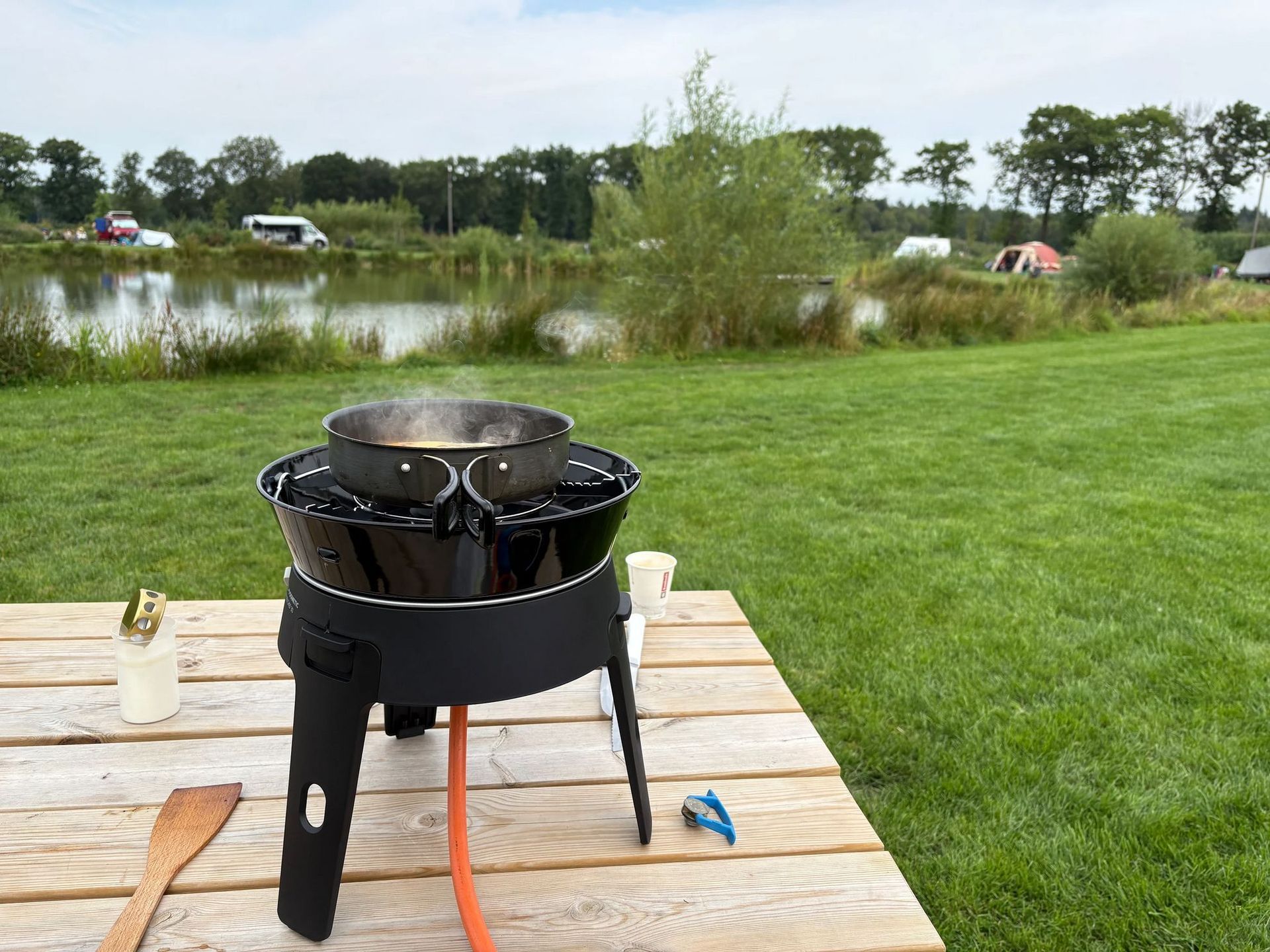 Kookpot op een kampeerfornuis op een houten tafel bij een meer.