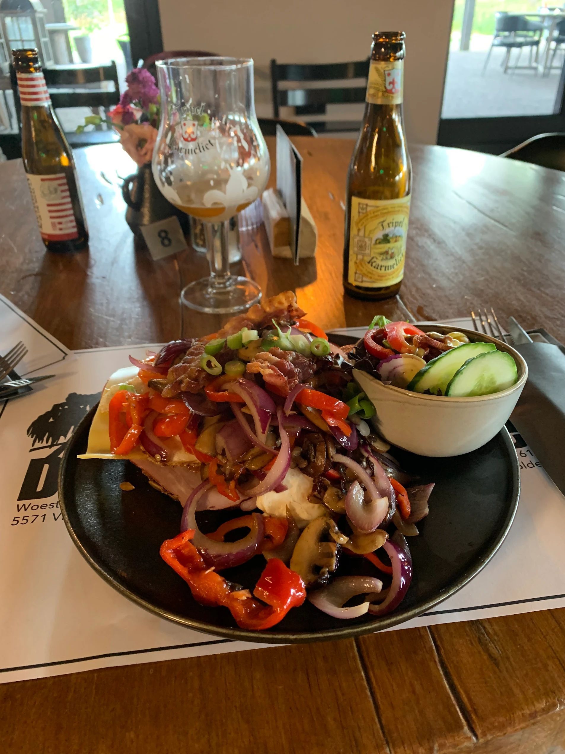 Bord met eten, salade, bierfles en glas op een houten tafel.