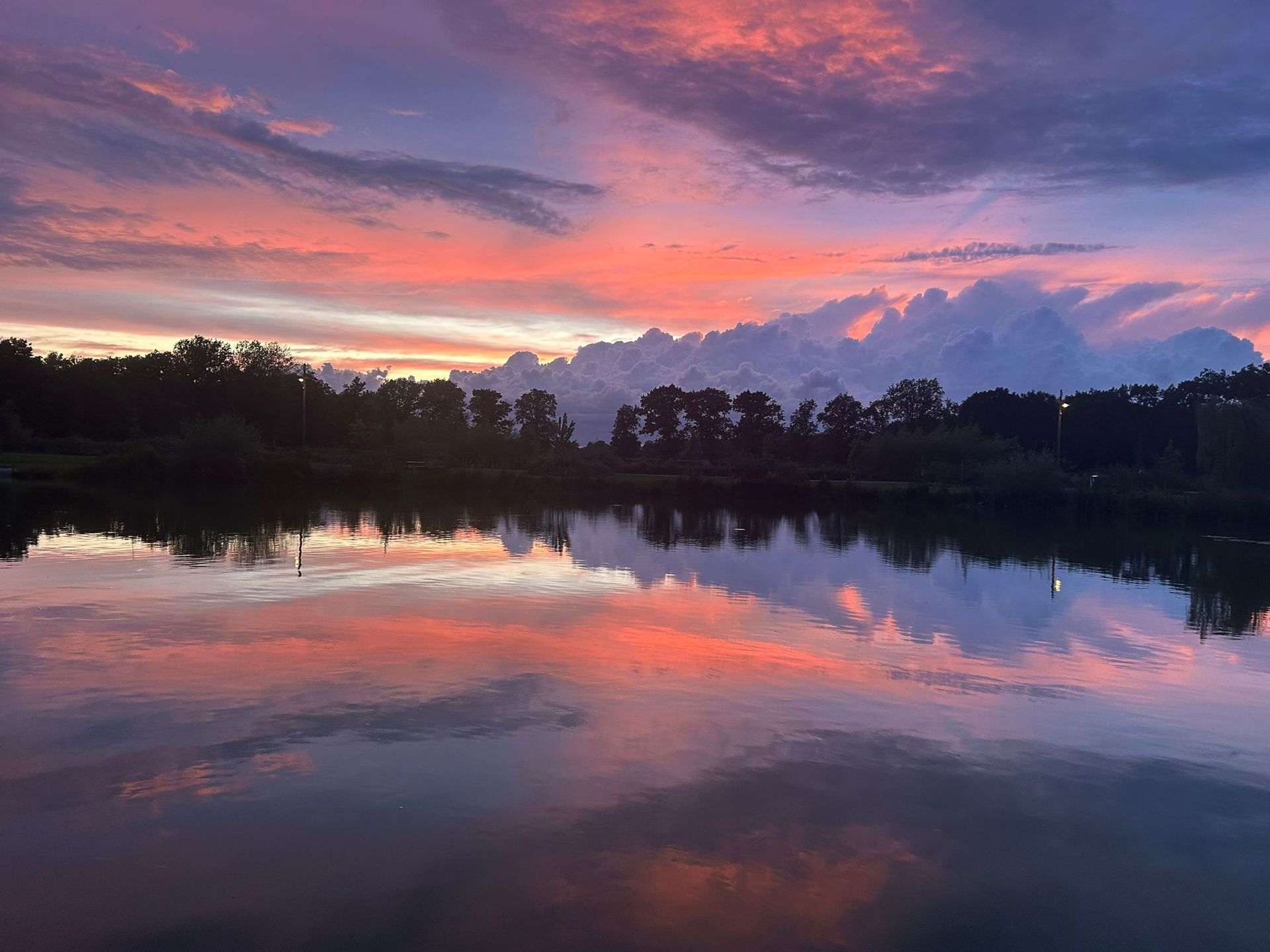 Zonsondergang boven een meer; oranje, roze en paarse lucht weerspiegeld in het stille water. 