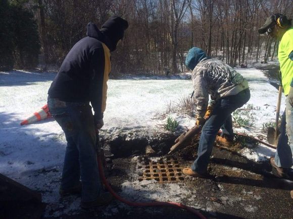 Three people tending a snowy outdoor fire pit with logs and smoke.