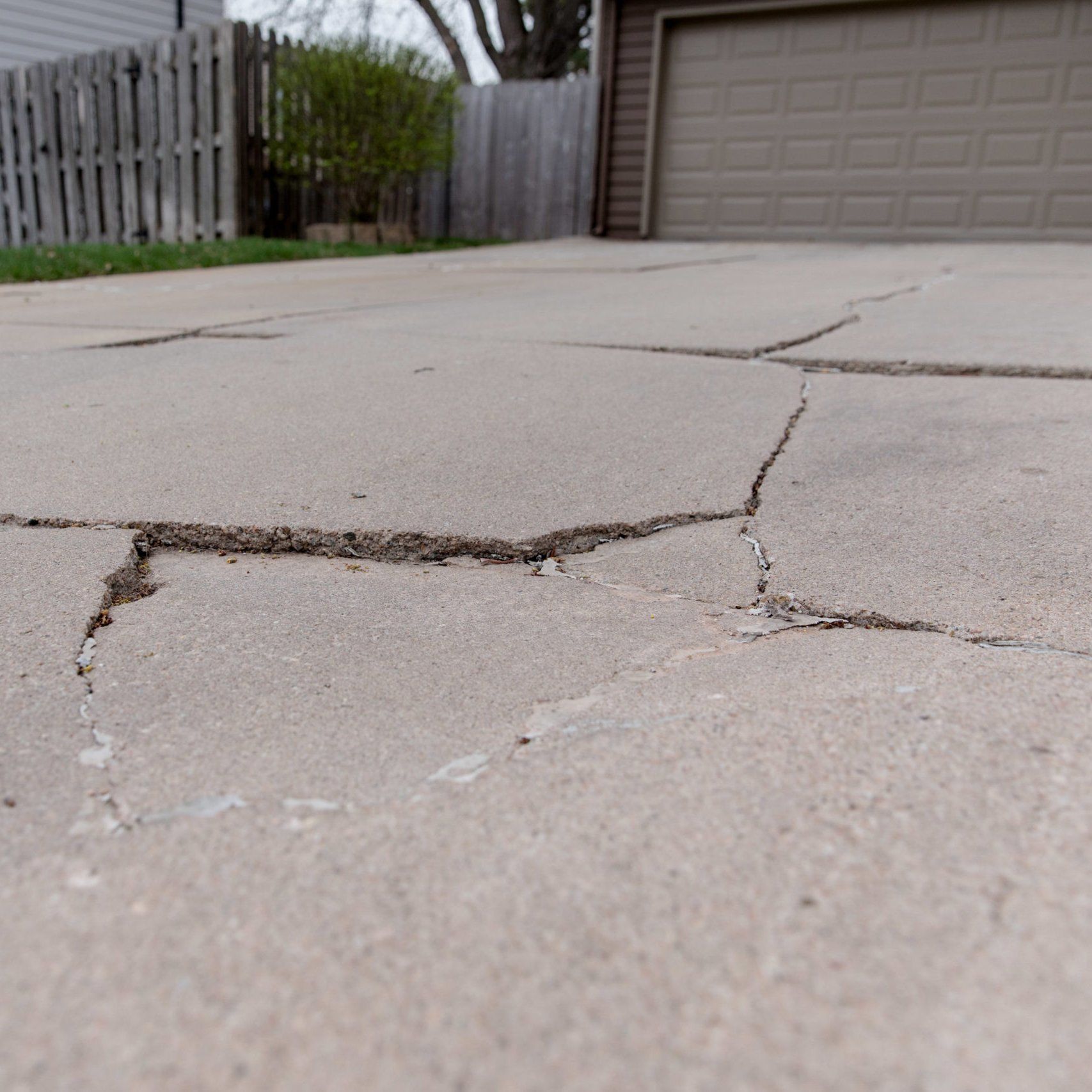 Cracked concrete driveway leading to a garage, with a wooden fence on the left.