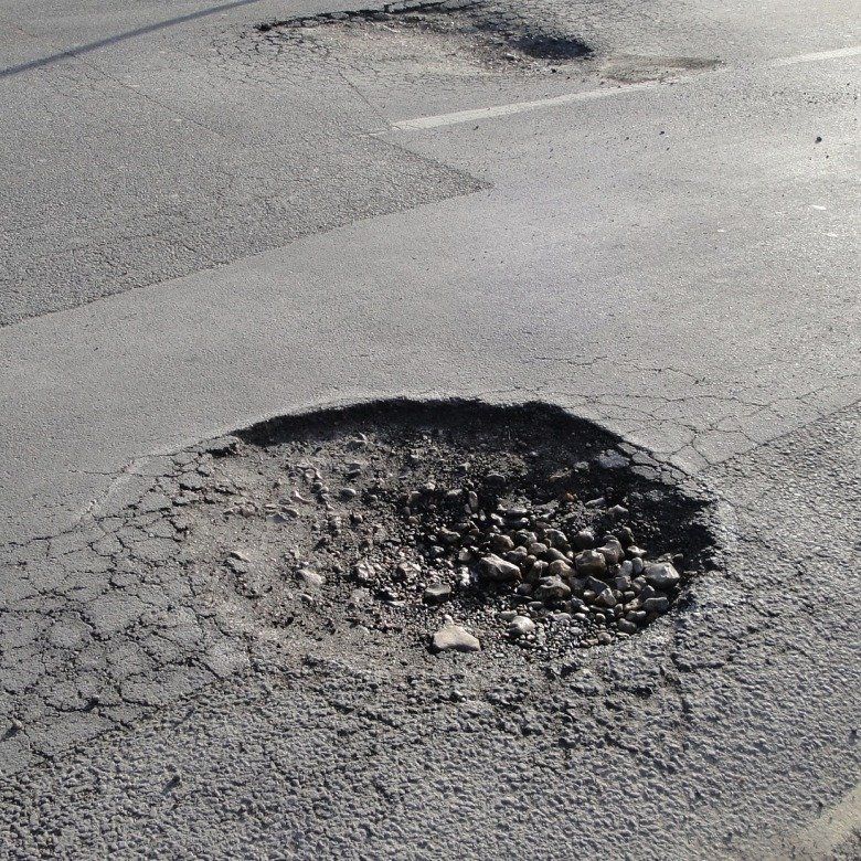 Damaged asphalt road with a large pothole and cracked pavement