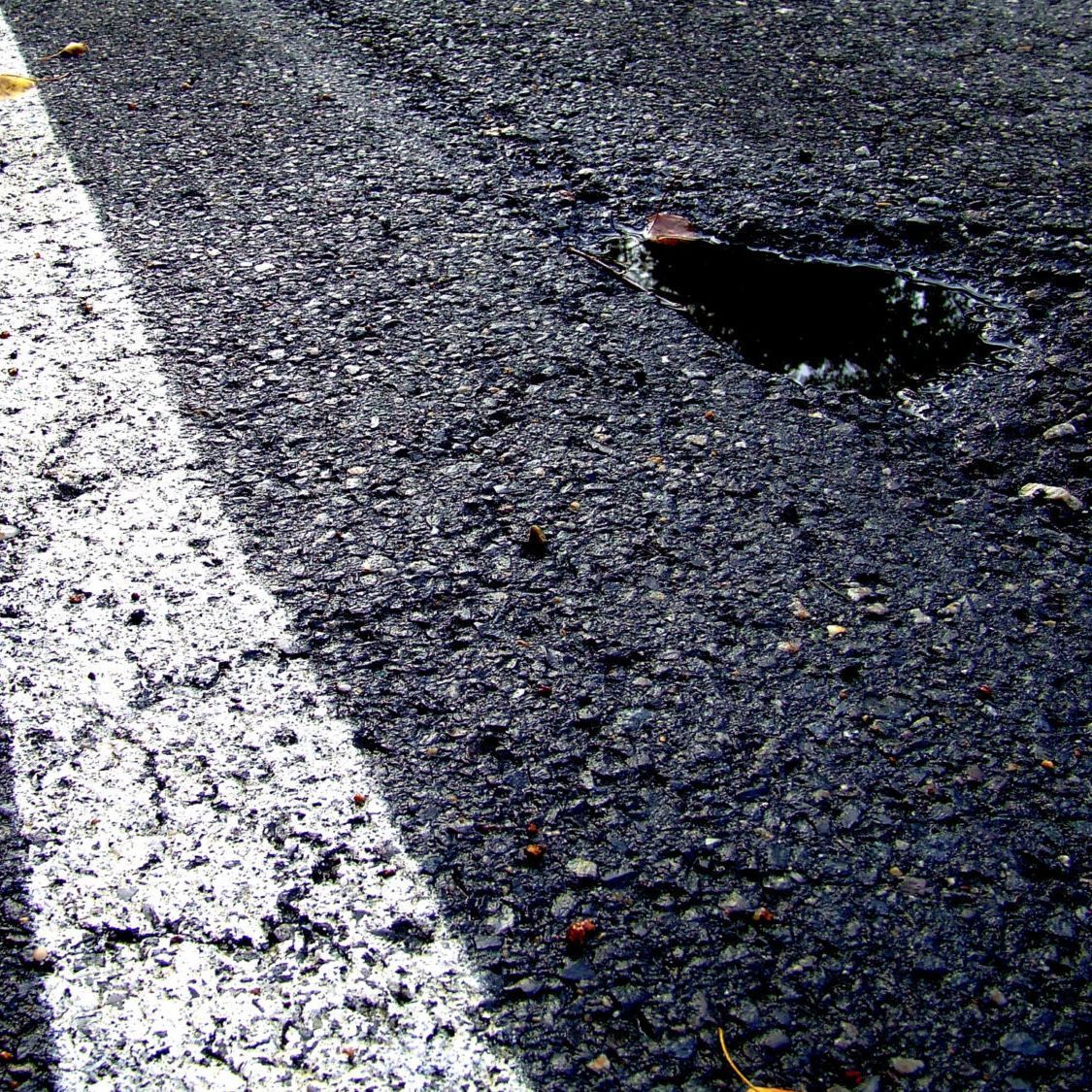 Cracked asphalt road with a pothole beside a white lane marking