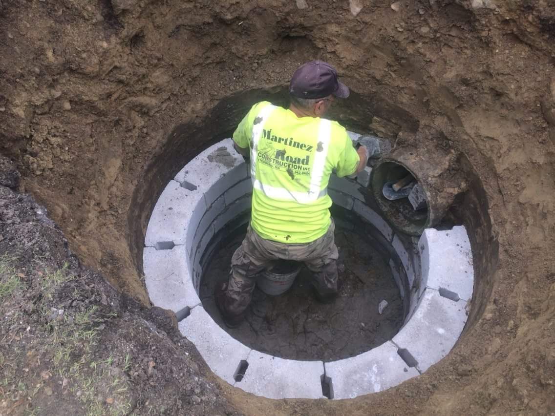 Worker in a neon vest standing inside a round underground utility shaft.