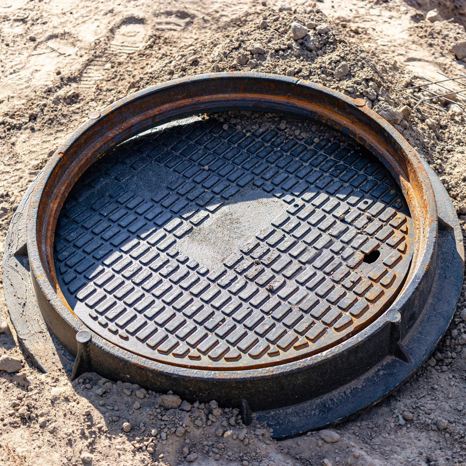 Round metal manhole cover on sandy ground, viewed from above.
