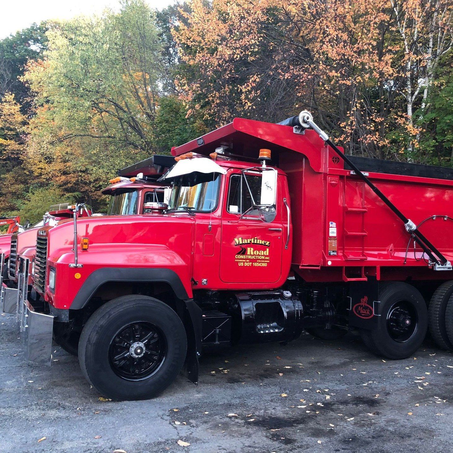 Red dump truck parked on gravel road with autumn trees in the background