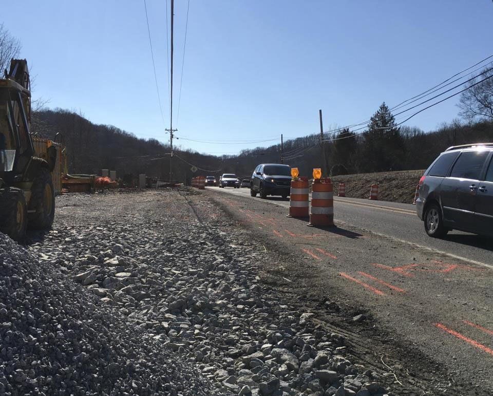 Road construction site with orange barrels beside a gravel shoulder and traffic passing on a sunny day