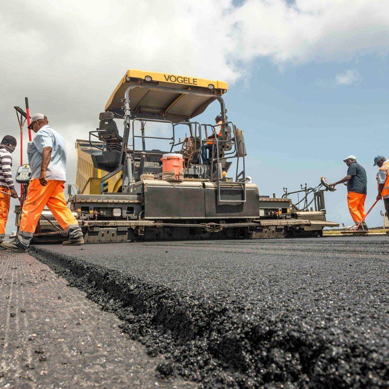 Road paving crew spreading fresh black asphalt with a yellow paver under a blue sky