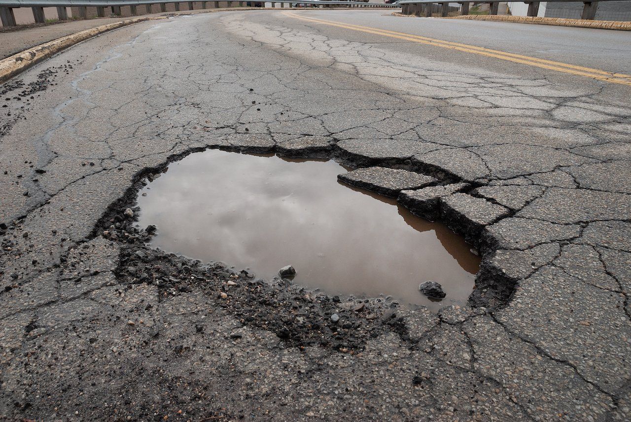 Large pothole filled with muddy water on a cracked asphalt road