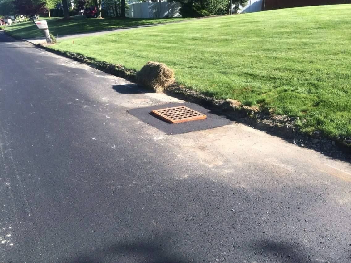 Street curb with storm drain beside a grassy lawn on a sunny day