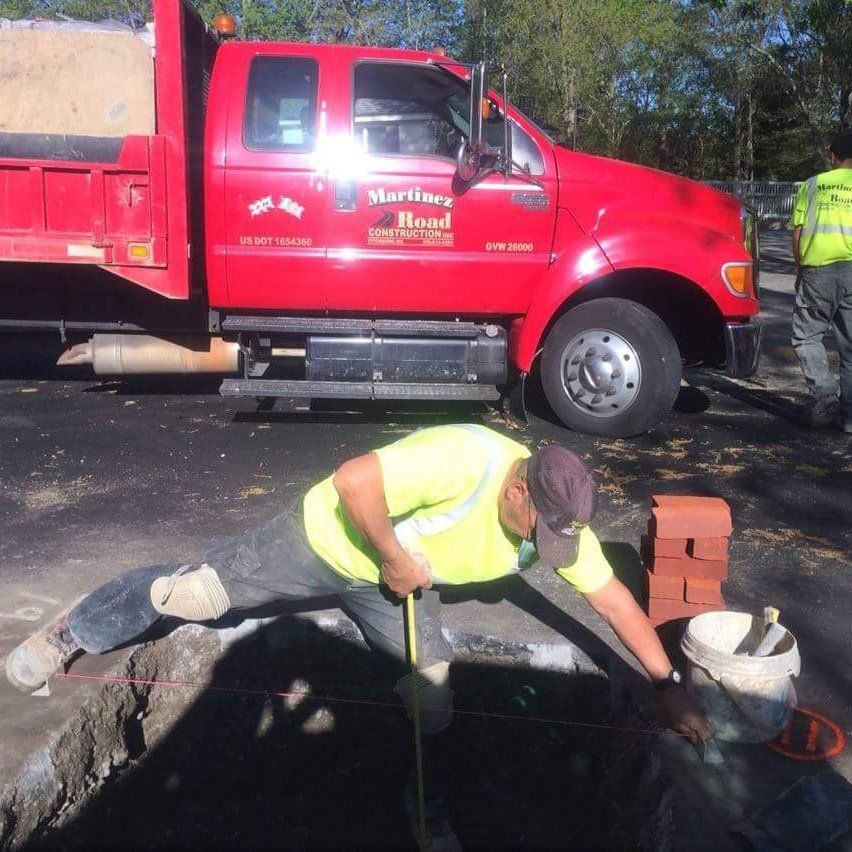 Worker in yellow vest repairs a water line beside a red utility truck.