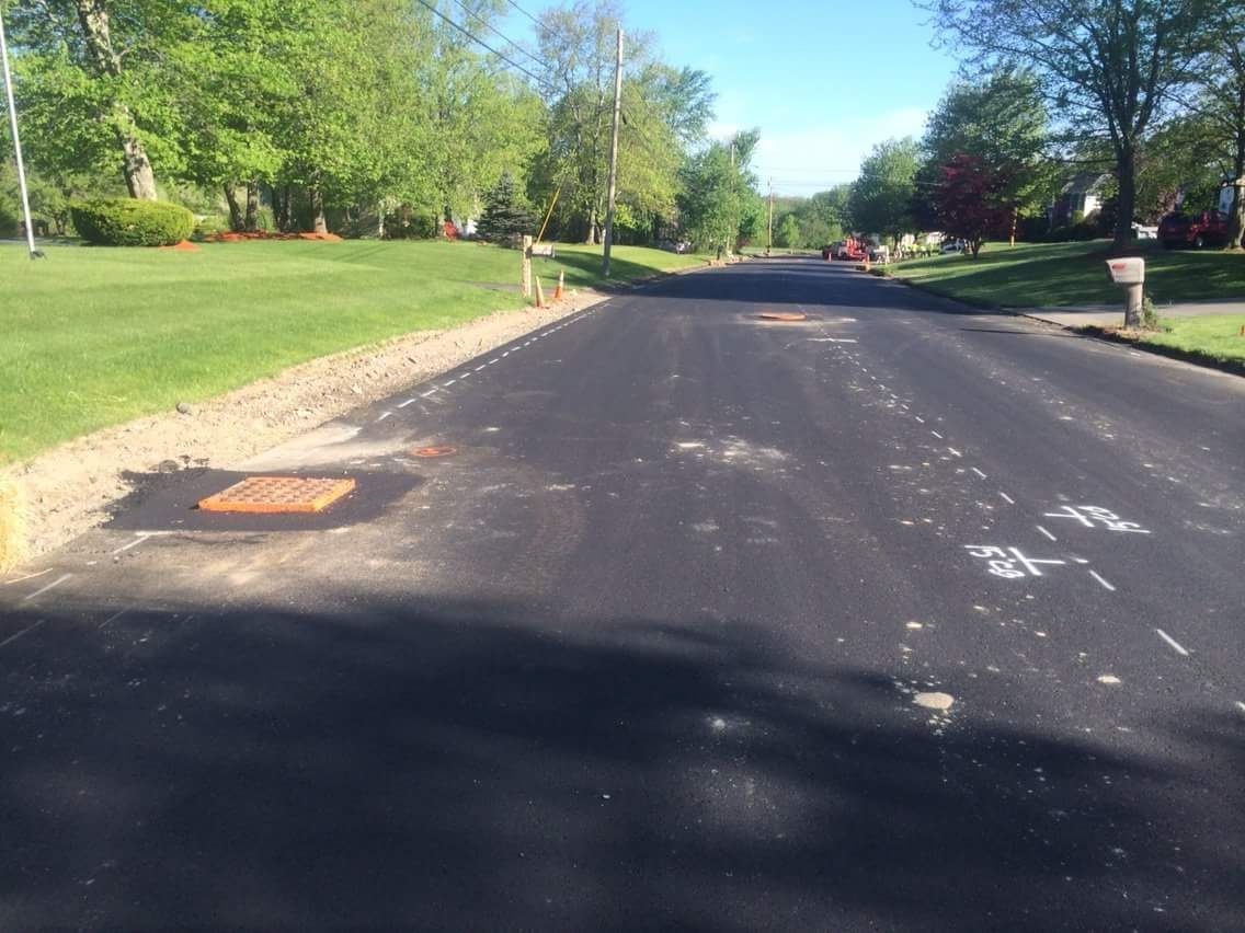 Quiet suburban road with fresh black asphalt, lined by green grass and trees on a sunny day