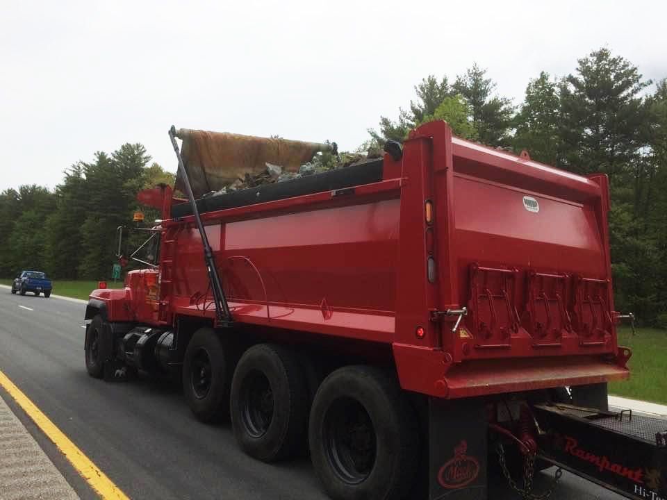 Red dump truck hauling debris on a highway, viewed from the rear side.