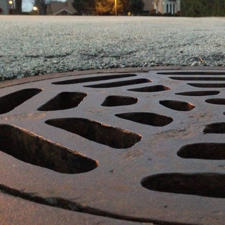 Close-up of a decorative metal storm drain cover on a frosty street at dusk