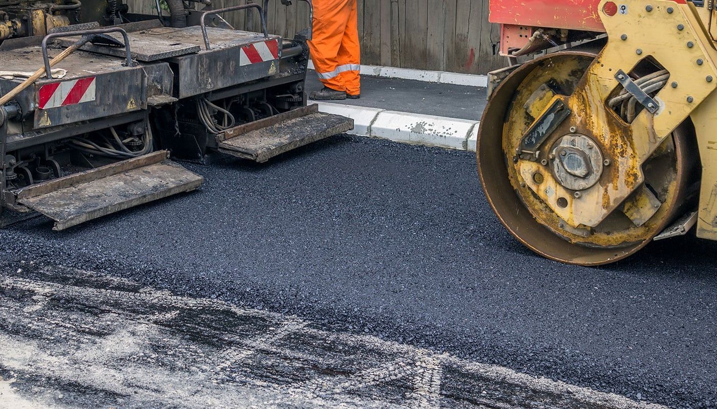 Road paving machine and roller compacting fresh black asphalt on a street repair site
