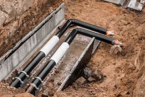 Trenched underground pipes with black and white insulation beside a concrete wall at a construction site