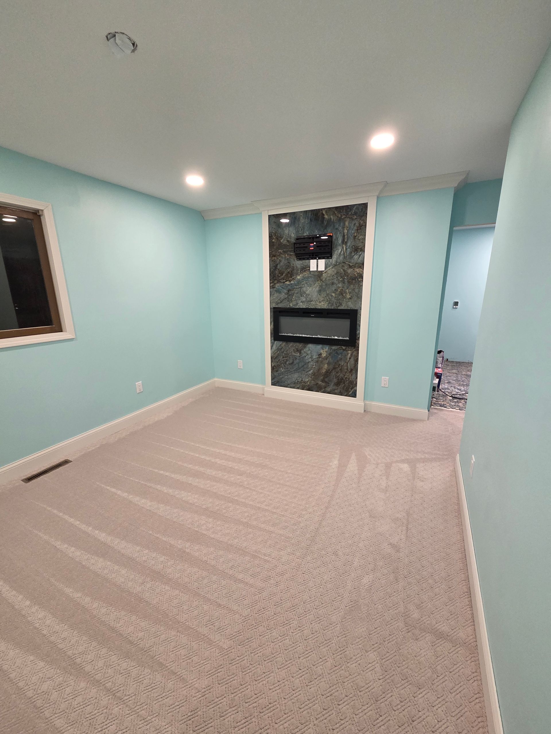 A room with light blue walls, tan carpet, and a dark marble-patterned fireplace feature wall with a built-in electric unit.