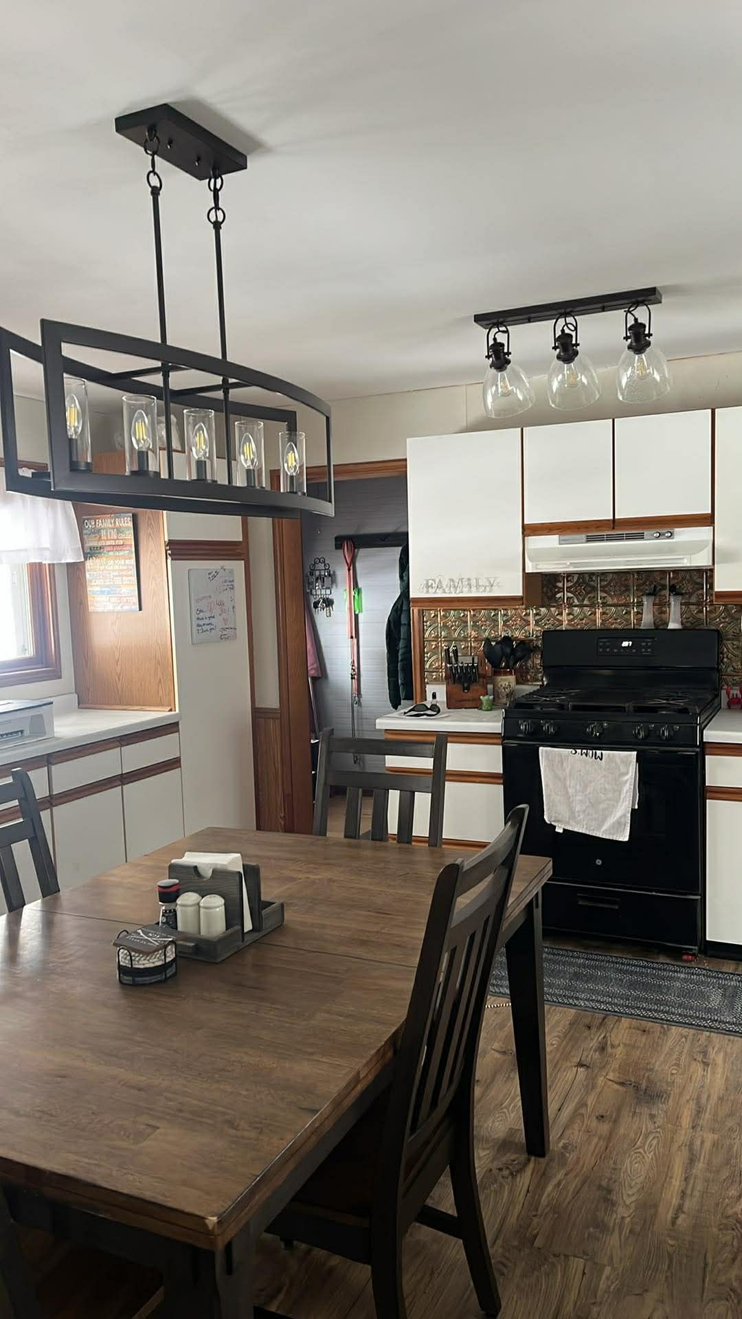 A dining room and kitchen featuring a dark wood table, matching chairs, overhead industrial lighting, and white cabinets.