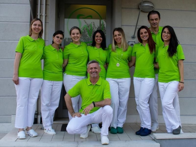 Gruppo di persone con camicie verde brillante e pantaloni bianchi in posa sui gradini di un edificio.