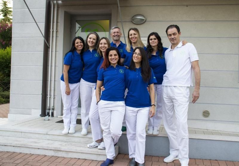 Tre membri dello staff sorridenti, con polo rosa e pantaloni bianchi, in piedi davanti all'ingresso di una clinica.