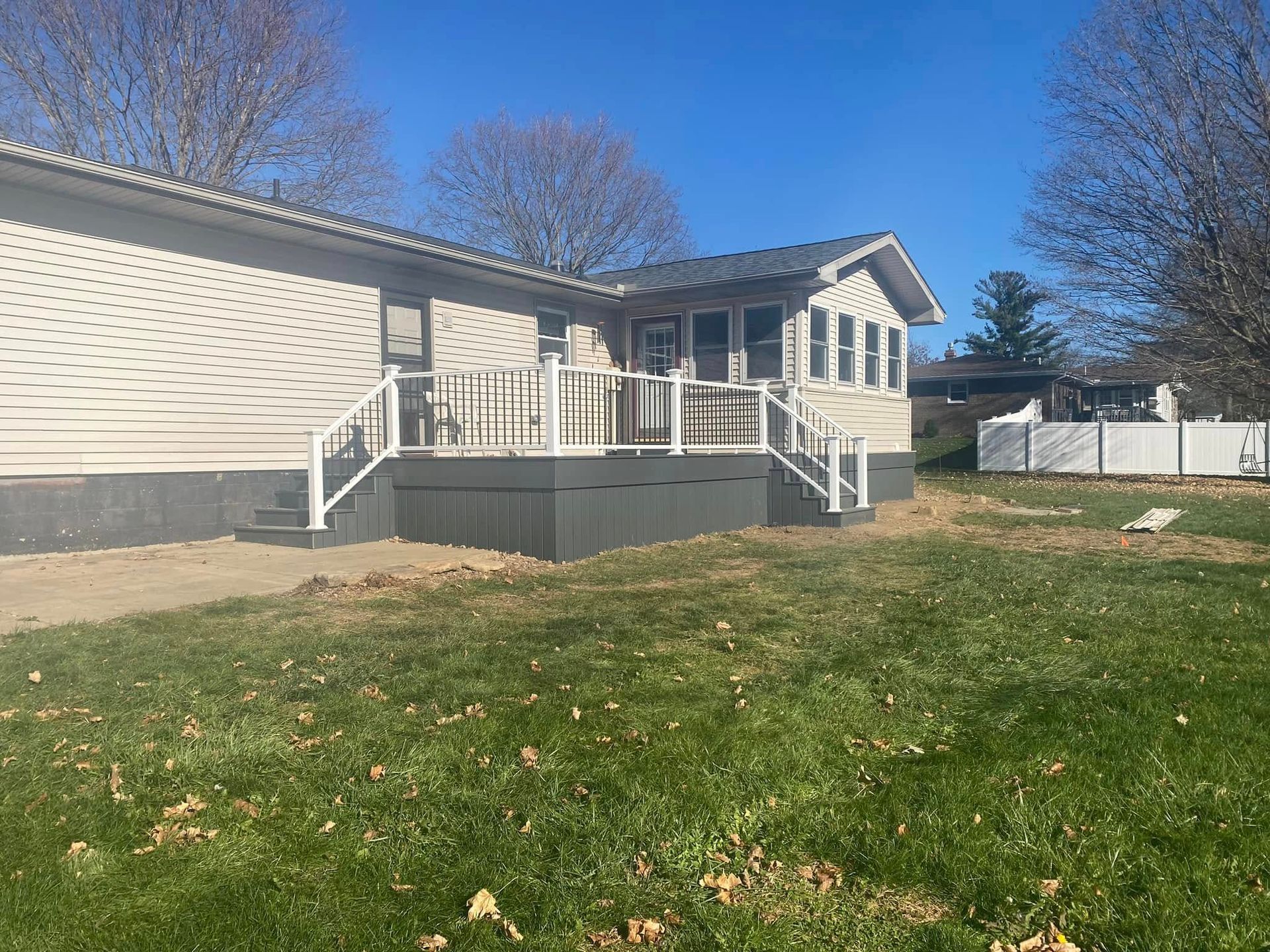 Single-story beige house with front porch and steps, surrounded by a grassy yard on a sunny day Single-story beige house with front porch and steps, surrounded by a grassy yard on a sunny day