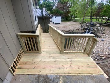 Wooden accessibility ramp and deck beside a house, with railings and a dirt yard beyond. Wooden accessibility ramp and deck beside a house, with railings and a dirt yard beyond.