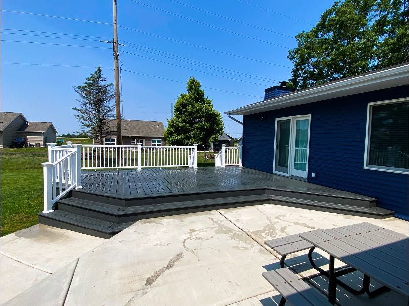 Backyard deck with white railing, blue house, and concrete patio under a clear sky Backyard deck with white railing, blue house, and concrete patio under a clear sky