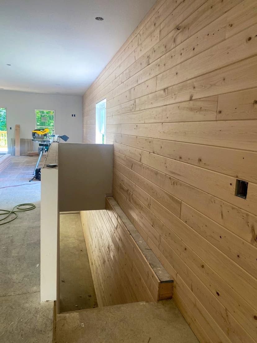 Long hallway under construction with wood-paneled wall, stair opening, and worker in the distance Long hallway under construction with wood-paneled wall, stair opening, and worker in the distance