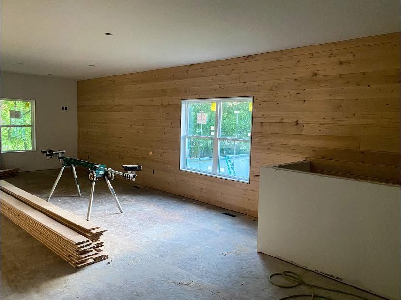 Partially finished room with wood-paneled walls, windows, and construction materials on the floor. Partially finished room with wood-paneled walls, windows, and construction materials on the floor.