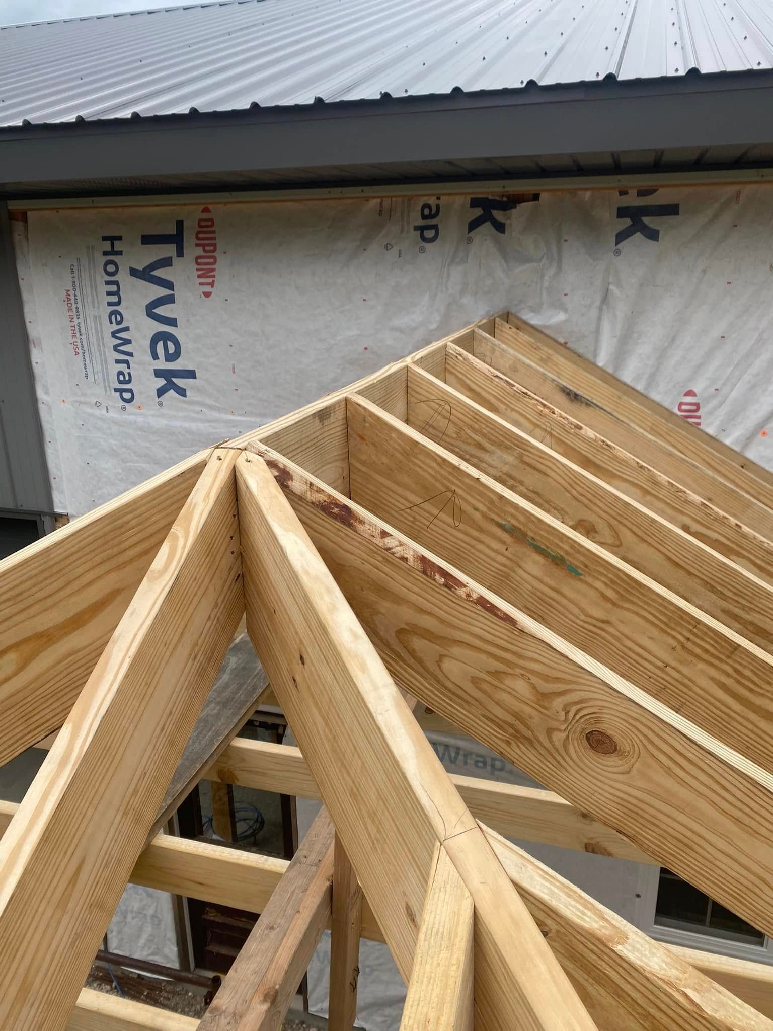 Wooden roof trusses under construction beside wrapped Tyvek house sheathing Wooden roof trusses under construction beside wrapped Tyvek house sheathing